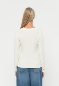 Long-sleeve, fitted knit sweater in cream, featuring a rounded neckline and smooth texture. Paired with loose, faded blue jeans.