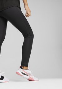 Leggings negros combinados con zapatillas deportivas blancas y rosas que presentan una parte superior texturizada y una suela de goma, con acentos en negro y rosa.