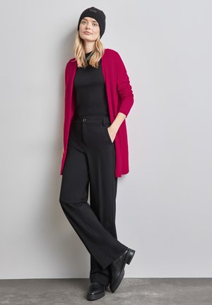 Black knit beanie, black fitted top, open fuchsia cardigan, black wide-leg trousers, and black shoes. Smooth textures and vibrant color contrast.