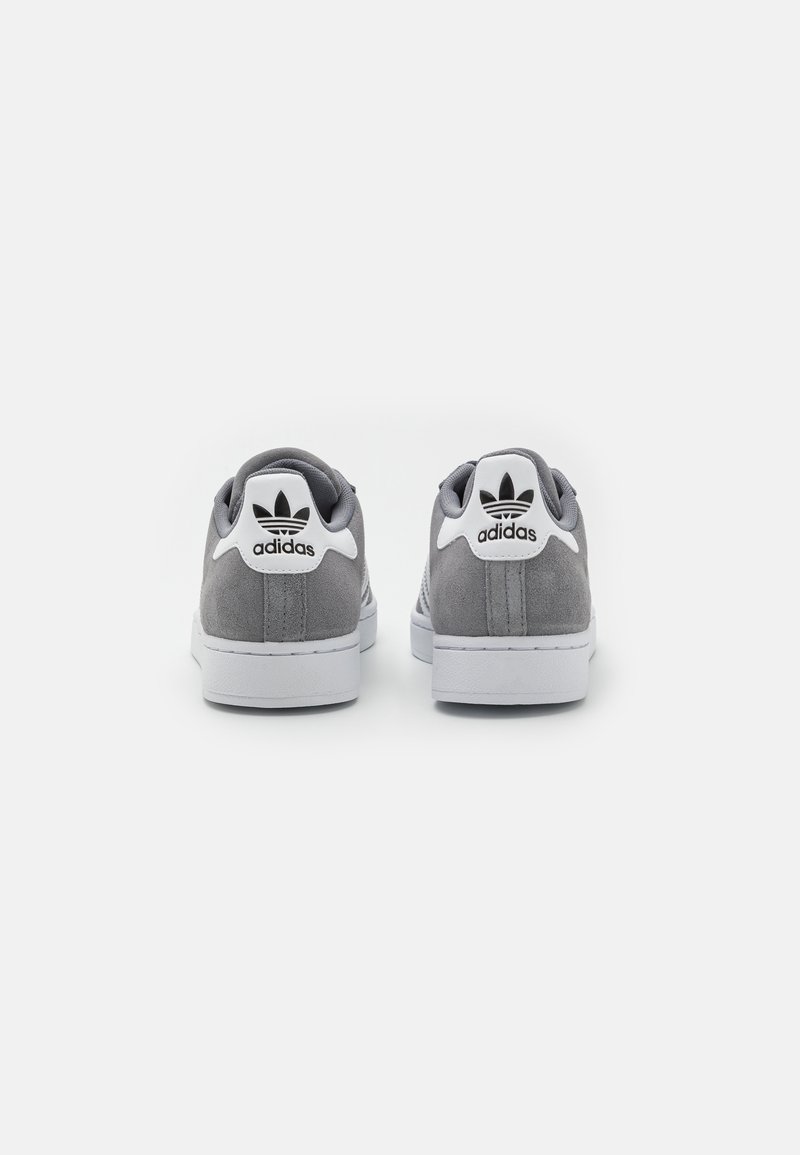 Graue Wildleder-Sneaker verfügen über eine weiße Gummisohle, texturierte Akzente und ein schwarzes Adidas-Logo mit einem Blattdesign an der Ferse.