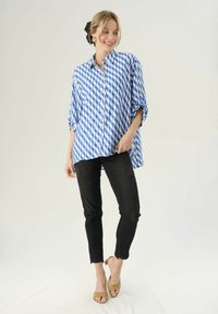 Niebieska i biała koszula w zygzakowy wzór z kołnierzykiem, zestawiona z czarnymi slim-fit dżinsami i beżowymi sandałami na obcasie.