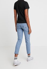 Camiseta negra de manga corta, vaqueros azul claro de talle alto con bajos deshilachados, zapatillas grises y calcetines blancos con rayas negras.