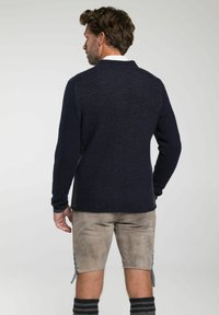 Marineblauer Strickpullover mit strukturiertem Finish und langen Ärmeln, kombiniert mit hellen Shorts, die seitliche Schnürdetails aufweisen.