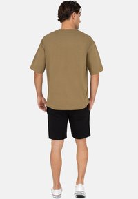 Oversized t-shirt in kaki met korte mouwen, gecombineerd met zwarte shorts en witte sneakers. Gladde textuur, eenvoudig ontwerp en een losse pasvorm.