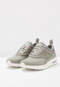 Sneaker atletiche grigio chiaro con tomaia in mesh e sintetico, punta arrotondata, chiusura con lacci e suola bianca imbottita. Marchio discreto su un lato.