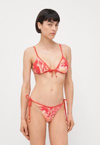 Bikini rosso con motivo floreale, caratterizzato da un top triangolare con dettaglio a fiocco al centro e laccetti laterali regolabili sul fondo.
