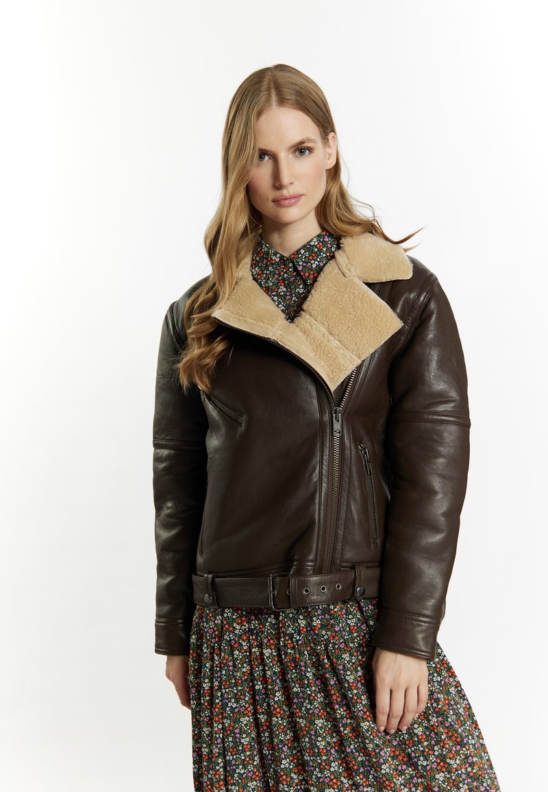 Giacca di pelle marrone con colletto in shearling beige. Caratterizzata da una chiusura con zip, tasche laterali e vita con cintura. Indossata sopra un abito floreale a fantasia.