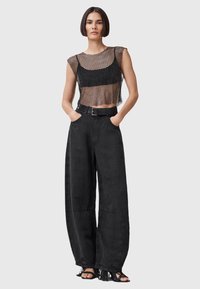 Czarny siatkowy crop top z krótkimi rękawami, w połączeniu z luźnymi czarnymi spodniami o szerokich nogawkach z paskiem i frędzlami.