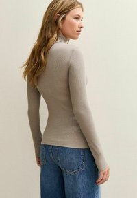 Langdurig gebreide top met lange mouwen in licht taupe, met een hoge hals. Gepaard met losse blauwe denim jeans. Zachte textuur en aangesloten ontwerp.