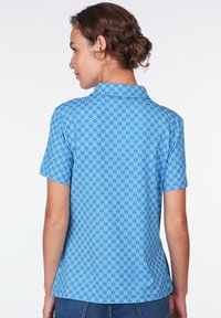 Kurzärmliges Poloshirt in Blau mit einem wellenförmigen geometrischen Muster. Aus weichem Stoff gefertigt, mit einem traditionellen Kragen und einer figurbetonten Silhouette.