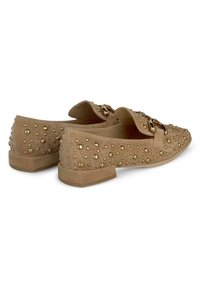 Beige Wildleder Slipper mit goldenen Nieten, flachem Absatz und runder Zehenpartie. Dekorative Schnallen-Details an der Vorderseite.