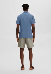 Kortärmad, ljusblå skjorta med krage, tillsammans med ljusgrå shorts. Skjortan har en slät textur och rak passform. Bruna sandaler.