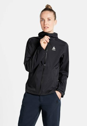 Black weather-resistant jacket with a hood, full zipper, and logo detail on the chest; paired with navy outdoor pants featuring pockets.