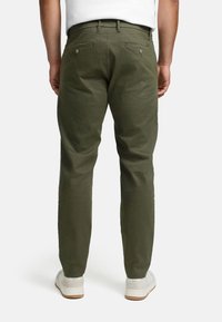 Pantalon chino vert olive à coupe droite, doté de deux poches arrière avec fermetures à boutons et fabriqué en coton. Associé à des baskets blanches.
