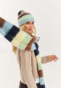 Dzianinowa wełniana czapka i dopasowany szalik w pastelowe paski w kolorach niebieskim, zielonym, żółtym i brązowym. Szalik ma wzór w kratę i teksturowane wykończenie.