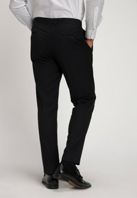 Pantaloni neri con una vestibilità slim, tessuto liscio e due tasche posteriori. Indossati con scarpe nere lucide. Camicia bianca parzialmente visibile in vita.