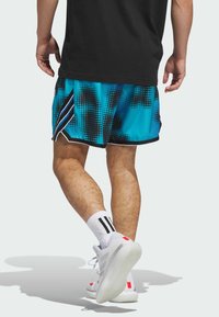 Shorts de sport courts à motif à pois bleu et noir, avec des rayures latérales noires. Portés avec des baskets blanches avec des accents rouges et des chaussettes noires.