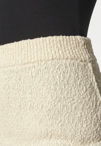 Jupe en tricot de couleur crème présentant un motif texturé et une taille côtelée. Le matériau semble doux et extensible, adapté au confort.