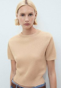 Beige short-sleeve knit sweater with a crew neck, featuring a ribbed texture and fitted silhouette. Worn with high-waisted jeans.