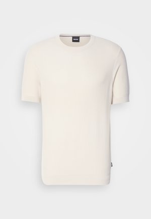 T-shirt a maniche corte di colore crema in maglia, con scollatura rotonda, caratterizzato da un tessuto testurizzato e un piccolo tag con logo sull'orlo.