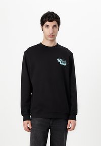 Zwarte sweatshirt van katoen, met een lichtblauw "Tommy Jeans" logo op de linkervoorzijde. Ribgebreide manchetten en zoom. Recht model.