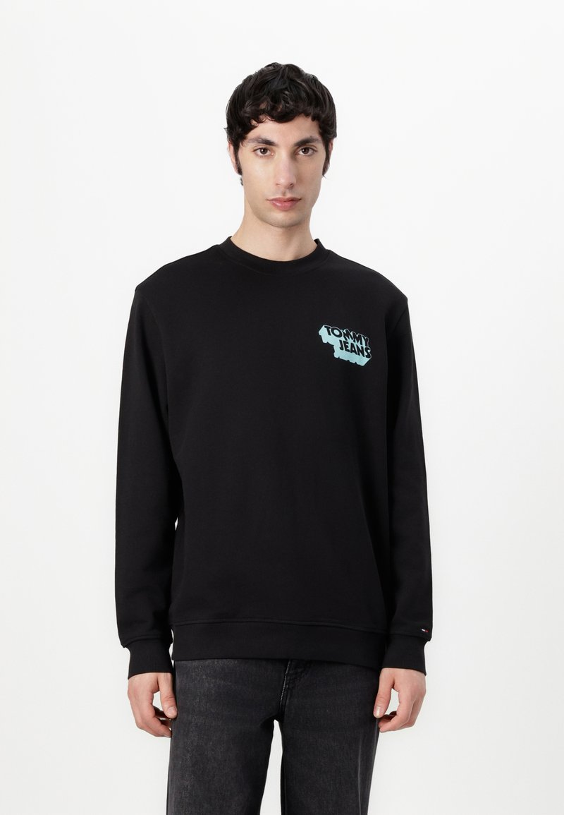 Zwarte sweatshirt van katoen, met een lichtblauw "Tommy Jeans" logo op de linkervoorzijde. Ribgebreide manchetten en zoom. Recht model.