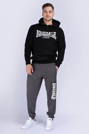 Fekete kapucnis felső fehér "LONSDALE LONDON" logóval, szürke melegítónadrággal párosítva, rajta fehér "ONSDALE" felirattal és rugalmas mandzsettákkal. Fehér sportcipő.