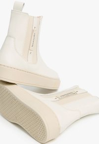Weiße Lederstiefeletten mit elastischen Seiteneinsätzen, einem dezenten Logo-Tag und strukturierten Gummisohlen mit Zickzackmuster.