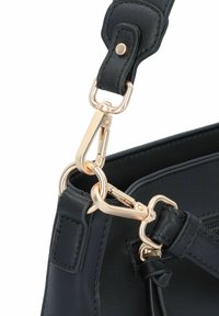 Details einer marineblauen Leder-Handtasche mit einem Verschluss und Beschlägen in Goldoptik, ausgestattet mit einem strukturierten Tragegurt und glatter Oberfläche.