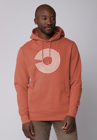 Roestkleurige hoodie met een groot wit cirkelvormig streepdessin aan de voorkant. Het heeft een capuchon met trekkoord en een voorzak in kangoeroestijl.