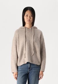 Felpa a maglia leggera beige chiaro con una vestibilità ampia, polsini a costine e un cordino. Indossata con jeans blu a gamba affusolata, con orlo corto e una consistenza morbida.