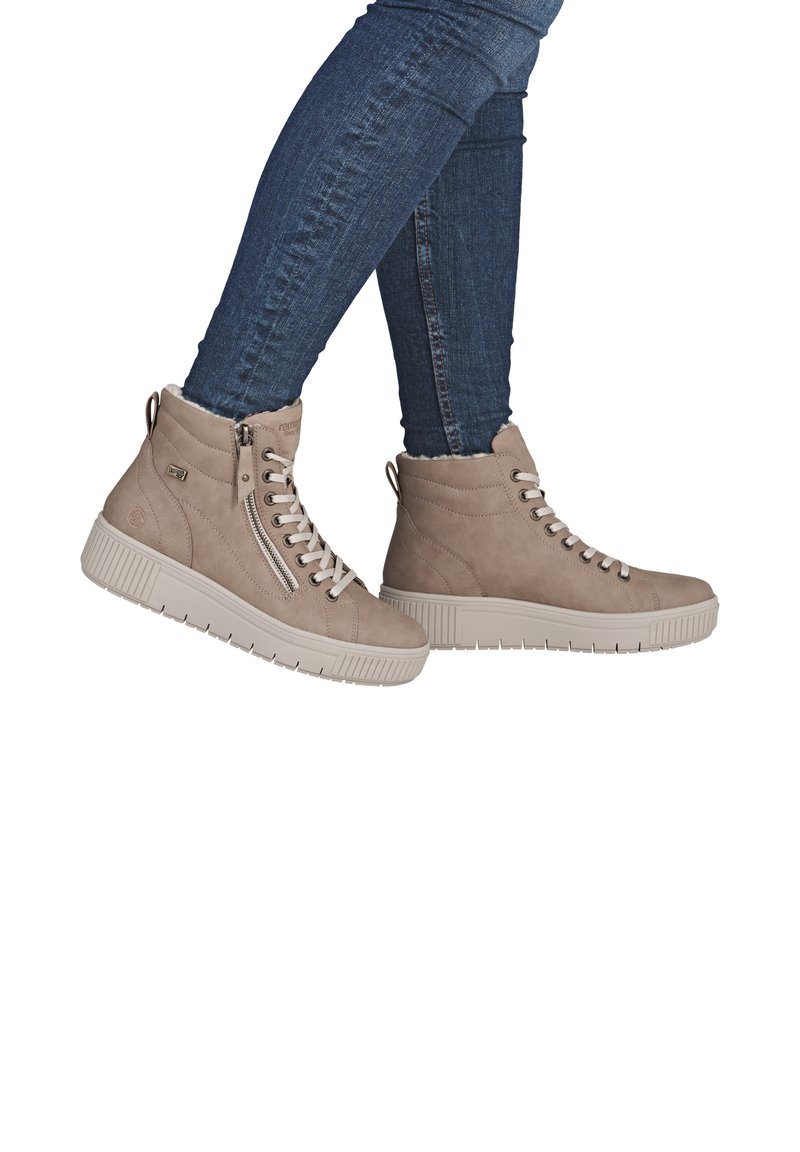 Beige suède enkellaarzen met een gestructureerde afwerking, voorzien van een zijrits en vetersluiting, gecombineerd met blauwe denim jeans.