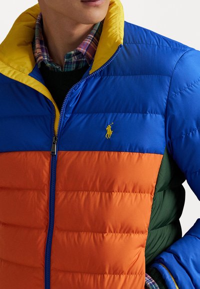 Puffer bunda s modrými, oranžovými a žltými panelmi, so zipsom a horizontálnym šitím. Obsahuje malé logo na hrudi.