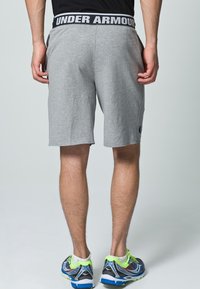 Šedé sportovní šortky z bavlněné směsi s kontrastním černým elastickým páskem s nápisem "UNDER ARMOUR" a malým logem.