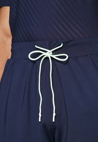 Tummansinisen väriset shortsit, joissa on elastinen vyötärö. Varustettu vaaleanvihreällä nyörillä, joka on solmittu rusetille. Kangas näyttää sileältä ja siinä on hillittömät pystysuuntaiset raidat.