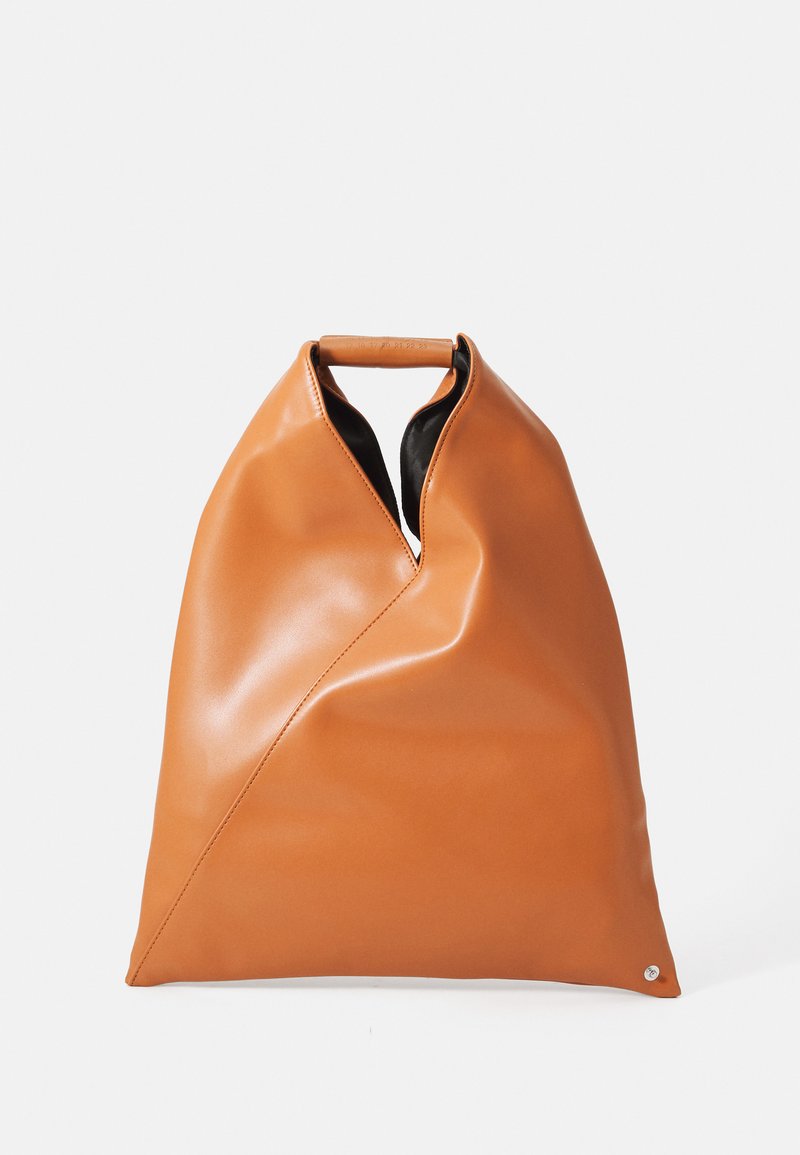 Läderväska i tanfärg med triangulära veck, topphandtag och svart inredning mot en enkel vit bakgrund.