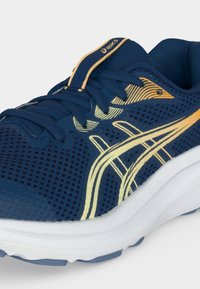 Μπλε και κίτρινο παπούτσι τρεξίματος Asics με διχτυωτό επάνω μέρος, κορδόνια και λευκή μαλακή σόλα, εμφανιζόμενο σε κλεινή γωνία.