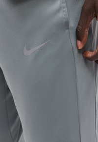 Κοντινό πλάνο χεριού ενός ατόμου κοντά στην πλαϊνή τσέπη γκρι παντελονιών Nike με εμφανές λογότυπο Nike swoosh.