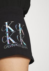 Černé bavlněné šortky s ribbovaným pasem a vícebarevným reflexním logem "CK" s textem "CALVIN KLEIN JEANS" na lemu.