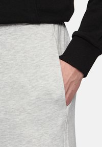 Grijze sweatpants met een zijzak, voorzien van een zachte textuur. Een zwart shirt met lange mouwen en geribde manchetten maakt de look compleet.