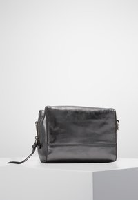 Czarna skórzana torba o prostokątnym kształcie, gładkiej fakturze i subtelnym połysku. Wyposażona w zamek błyskawiczny i boczny pasek dla większej wszechstronności.