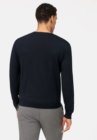 Donkerblauwe gebreide trui met een ronde halslijn en lange mouwen, voorzien van een geribde onderrand en manchetten, gecombineerd met grijze broek.