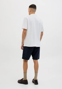 Polo bianco a maniche corte e dal taglio rilassato, abbinato a pantaloni cargo blu navy. Mocassini marroni e calzini marroni chiari completano il look.