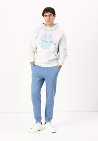 Sudadera de color gris claro con estampado de logo, combinada con pantalones de chándal azul claro. Tejido suave, ajuste relajado. Usado con zapatillas blancas.