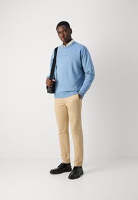 Lichtblauwe sweatshirt met een ronde hals, beige slim-fit chinos en zwarte veterschoenen. Draagt een zwarte schoudertas. Eenvoudig ontwerp.