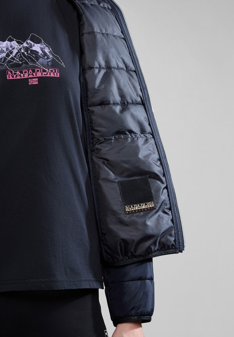 Kurtka Napa Puri z teksturowanym, ciemnoniebieskim rękawem typu puffer, z logo naszywką i gładkim, lekkim designem materiału.