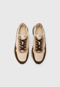 Baskets beige clair et marron avec une tige en daim et cuir, des lacets plats, une fermeture éclair sur le côté et une semelle en caoutchouc noir texturé.