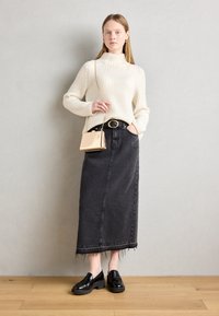 Kremowy sweter prążkowany z wysokim kołnierzem; czarna jeansowa spódnica maxi z postrzępionym dołem; czarne loafersy na platformie; mała torebka z złotymi akcentami.