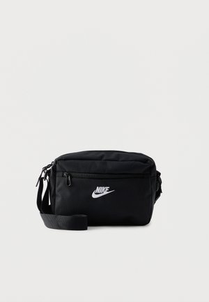 Geantă crossbody neagră Nike cu buzunar frontal cu fermoar, curea reglabilă și logo alb în față pe fundal simplu.