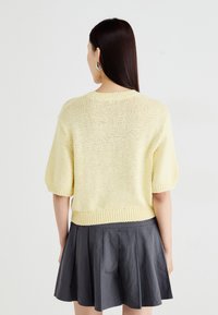 Sweater de malha de manga curta, amarelo claro, com bainha justa e ombros caídos, combinado com uma saia plissada escura.